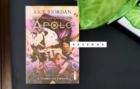 Livro físico de A Tumba do Tirano em cima de uma mesa preta com folhas passando por cima