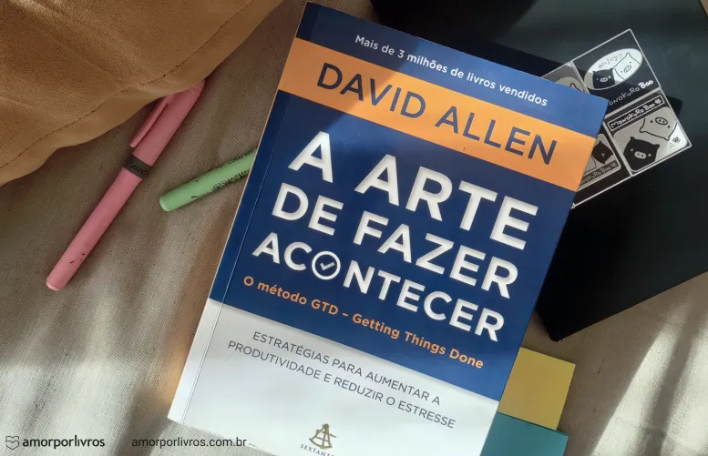 “Capa do livro ‘A Arte de Fazer Acontecer: O método GTD – Getting Things Done’, de David Allen, em destaque sobre uma superfície clara, com marcadores de texto coloridos ao lado.