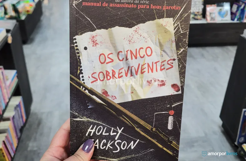 Uma mão segurando o livro Os Cinco Sobreviventes, de Holly Jackson