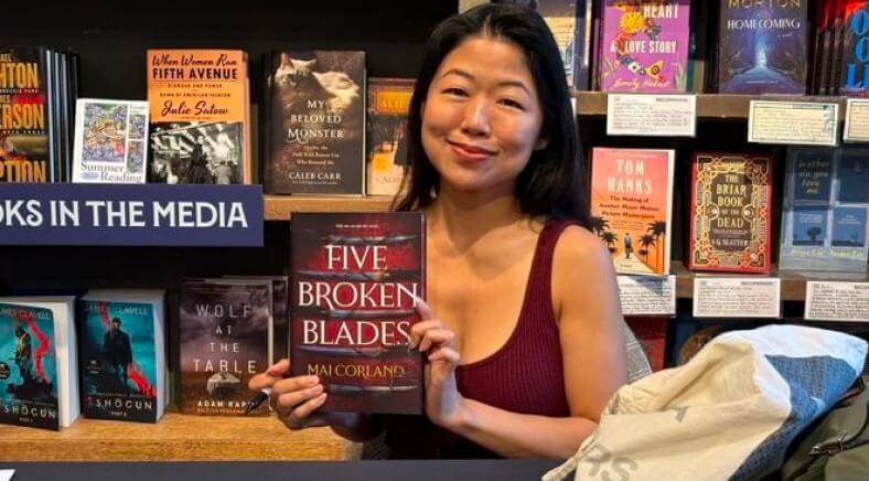 Mai Corland segurando seu livro Five Broken Blades